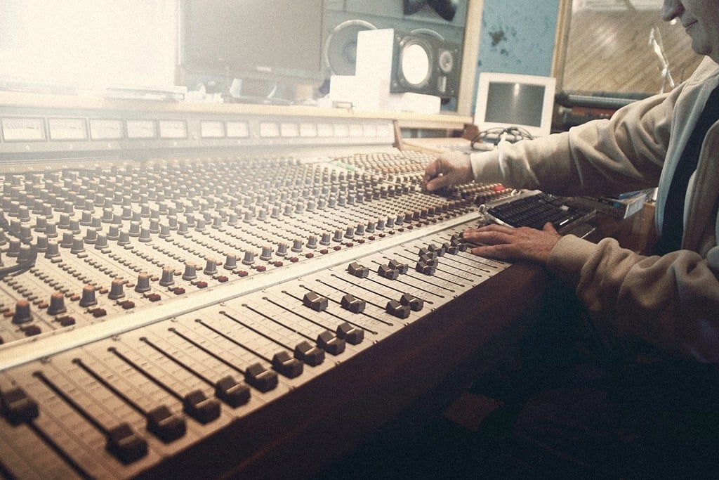 Hands working the faders of an analog mixing console in a recording studio