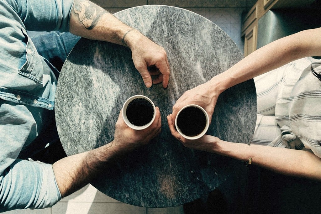 Two people seated across a small round table, each holding a cup of coffee