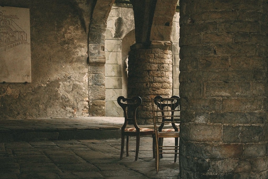 Two wooden chairs side by side beneath a stone archway